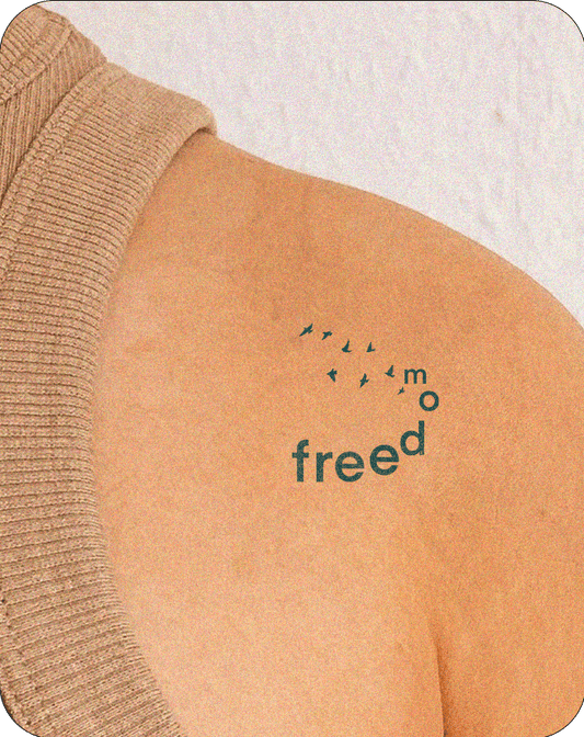 Semi-permanent tattoo on the shoulder featuring the word "freedom" with stylized letters rising upward, accompanied by silhouettes of birds flying, symbolizing liberation and movement.