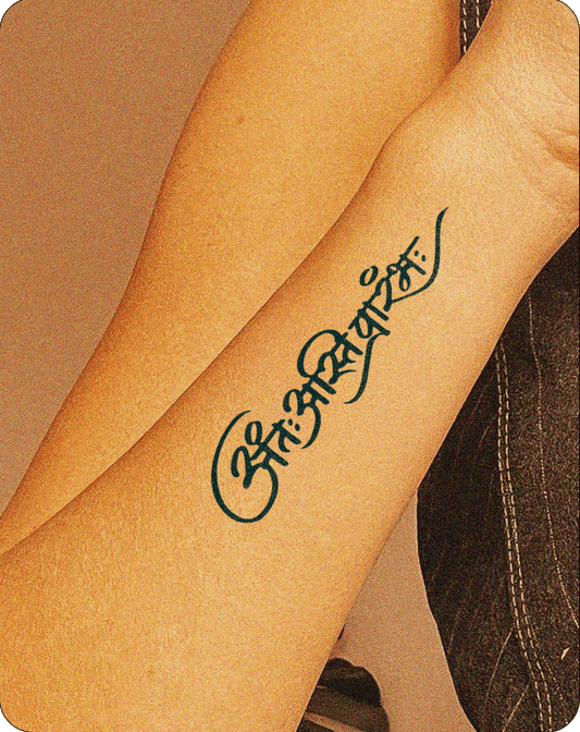 The image features a close-up of a forearm with a Sanskrit tattoo reading "ॐ नमः शिवाय," a sacred mantra dedicated to Lord Shiva. The tattoo is in a flowing, cursive script, inked in dark blue.
