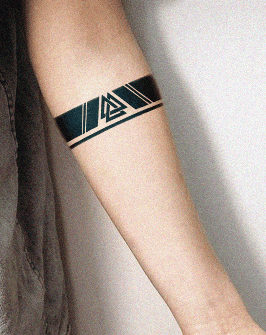 A forearm tattoo featuring a bold black armband design with a central Valknut symbol—three interlocked triangles—framed by angular geometric lines and bordered by two thin parallel bands, wrapping cleanly around the arm.