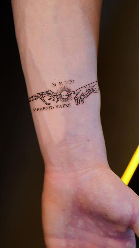A forearm tattoo inspired by Michelangelo’s "Creation of Adam," featuring two hands almost touching, symbolizing the connection between humanity and divinity. Above the hands, the phrase "MEMENTO VIVERE" (remember to live) is inked in an elegant font. This tattoo combines classical art with a powerful message of living in the present and embracing life.