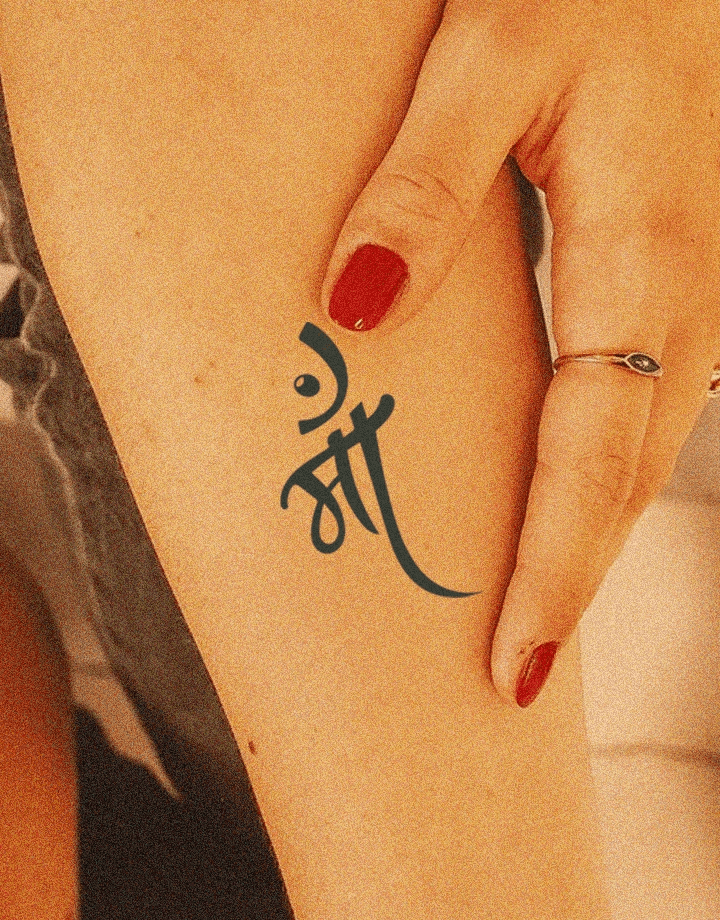 Black 'माँ' (Maa) tattoo in artistic Devanagari script on the upper thigh, symbolizing motherly love, with a hand resting near it