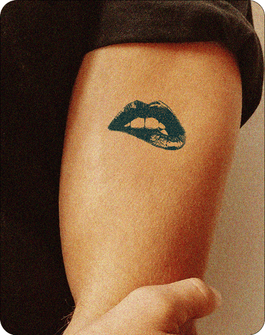 A dark , semi-permanent tattoo, suitable for Inkhub, is shown on a person's forearm. The tattoo depicts a stylized mouth with visible teeth and a slightly parted expression. The design has a bold, graphic quality against the person's skin.